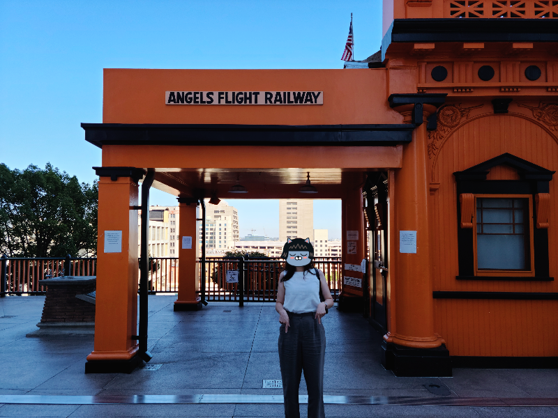 앤젤스 플라이트 앞에서 개인 사진을 찍었다. 주황색 건출물 위에 Angels Flight Railway라고 쓰여 있다. 