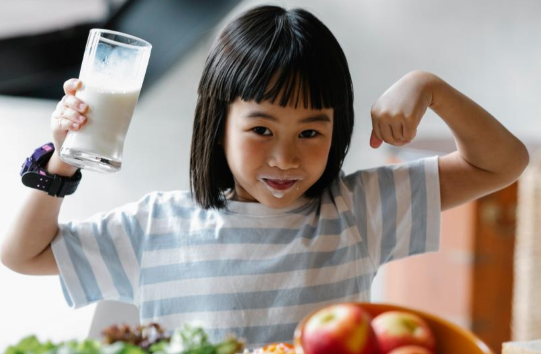 한 여자아이가 우유를 마쉰 뒤 웃고 있다.