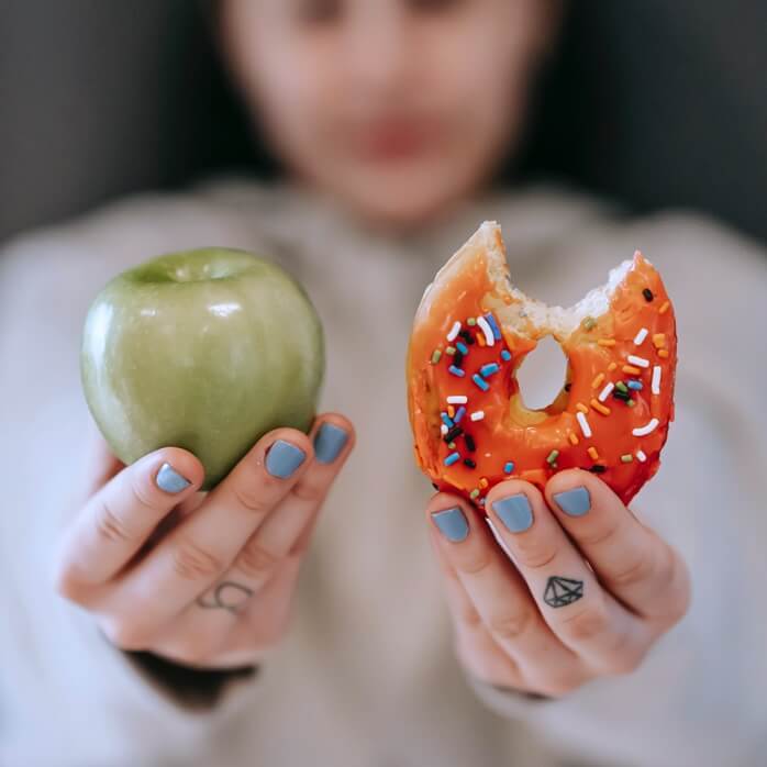 한 여자가 한 손에는 연두색 사과를&#44; 다른 한 손에는 한 입 베어먹은 도넛을 들고 있는 모습