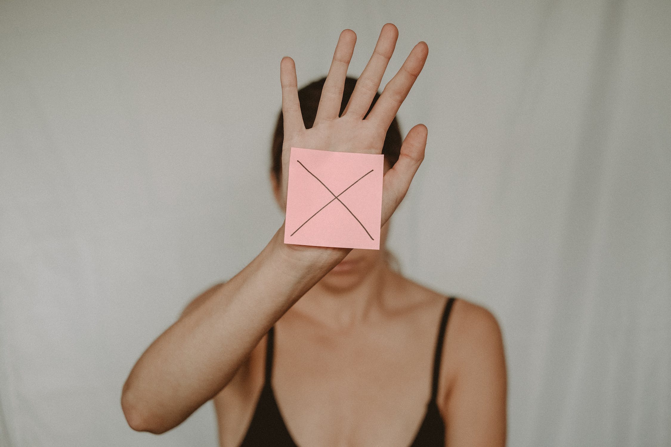 한 여자가 분홍색 포스트잇에 엑스를 그어 보여주고 있다.