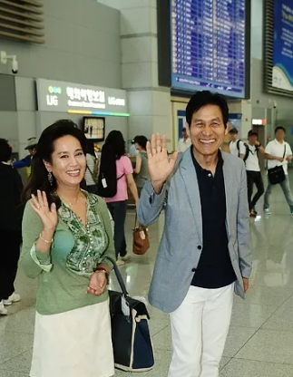 배우 안성기와 배우자 오소영이 공항에서 기자를 향해 손 인사를 하고 있다.