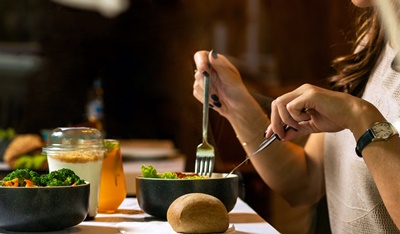 채소 음식 위주의 식탁에서 포크와 나이프를 들고 식사를 하고 있는 여성의 모습