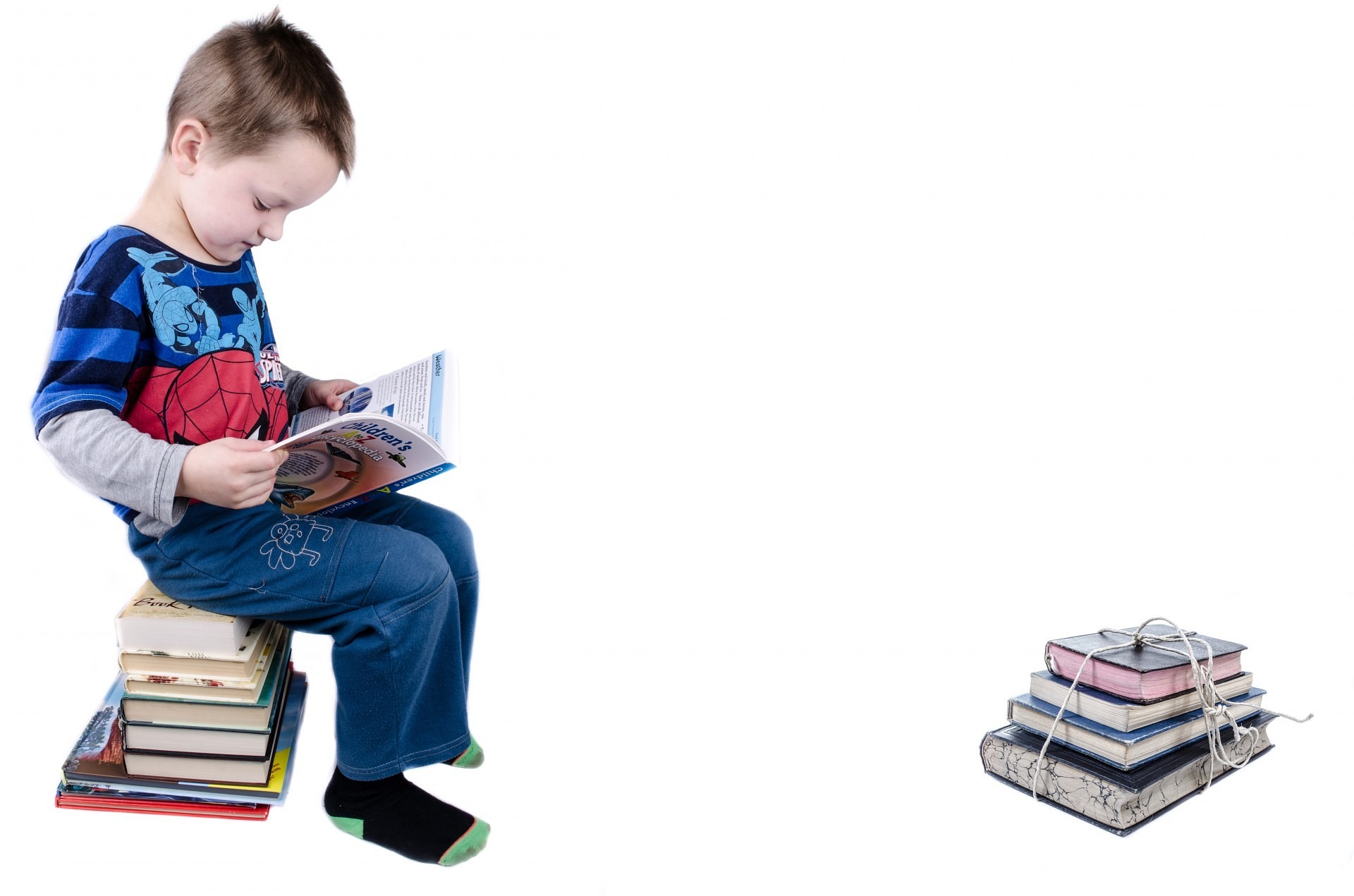 읽을 책들을 쌓아놓고 그 위에 앉아서 책을 읽고 있는 아이와 그 앞에는 다 읽은 책들을 끈으로 묶어 놓고 찍은 사진