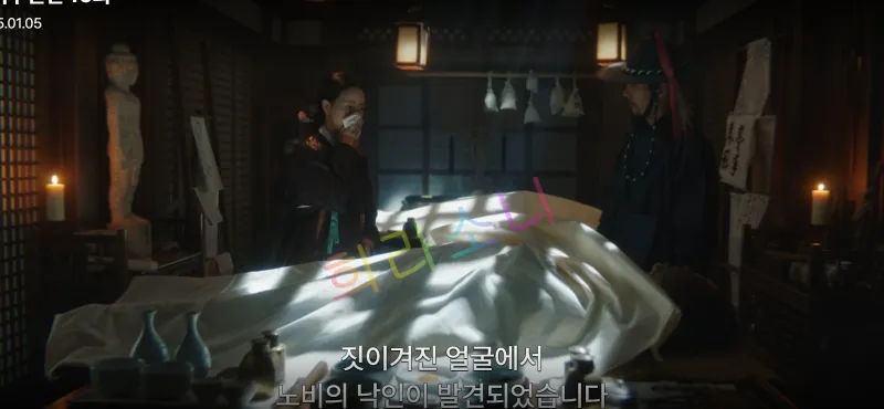 조명이 어둡고 차분한 분위기의 방 안&amp;#44; 하얀 천으로 덮인 시체 앞에서 두 사람이 서 있습니다. 태영은 코를 막고 있고 남자는 전통 복장을 입은 상태입니다. 자막은 &amp;quot;짓이겨진 얼굴에서 노비의 낙인이 발견되었습니다.&amp;quot;
