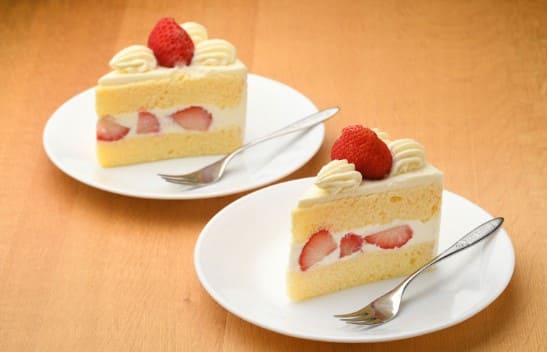 딸기 케이크가 흰색 접시위에 올려져 있고 옆으로 포크가 놓여져 있다