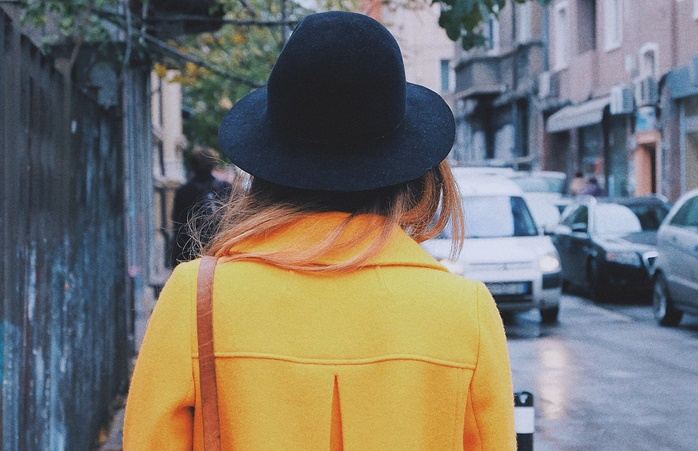 검은 모자를 쓰고 오렌지 색 코트를 입고 걷고 있는 여자의 뒷모습