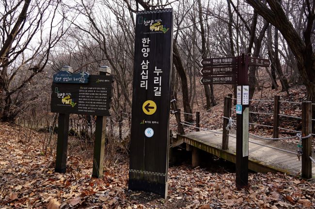 한양삼십리 누리길 길안내판&#44; 검은 바탕에 흰글씨&#44; 하단에 봉화길 안내 화살표&#44; 뒤로는 이배재 가는 계단길&#44;