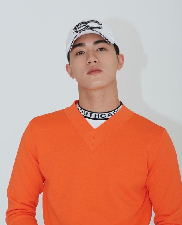 윤준혁이 오렌지색 골프셔츠를 입고 하얀 모자를 쓴 정면을 바라보는 사진