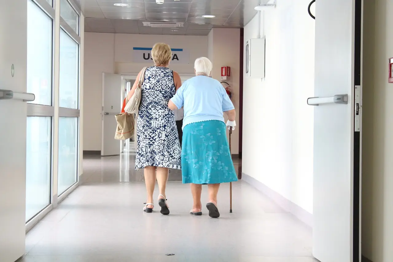 응급시-하얀 병원복도를 걸어가는 젊은여자와 지팡이를 짚은 할머니의 뒷모습