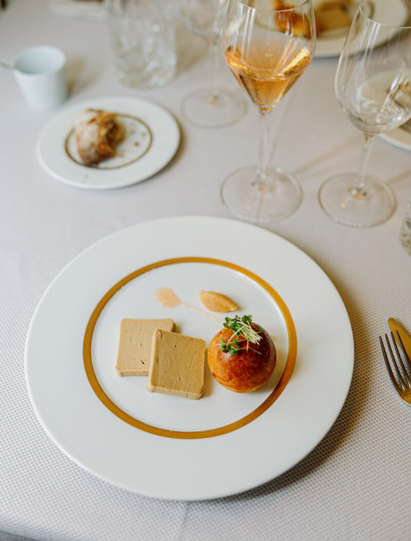 푸아그라가 접시에 놓여있고 접시 위쪽에는 노란 빛깔의 와인이 놓여있다.