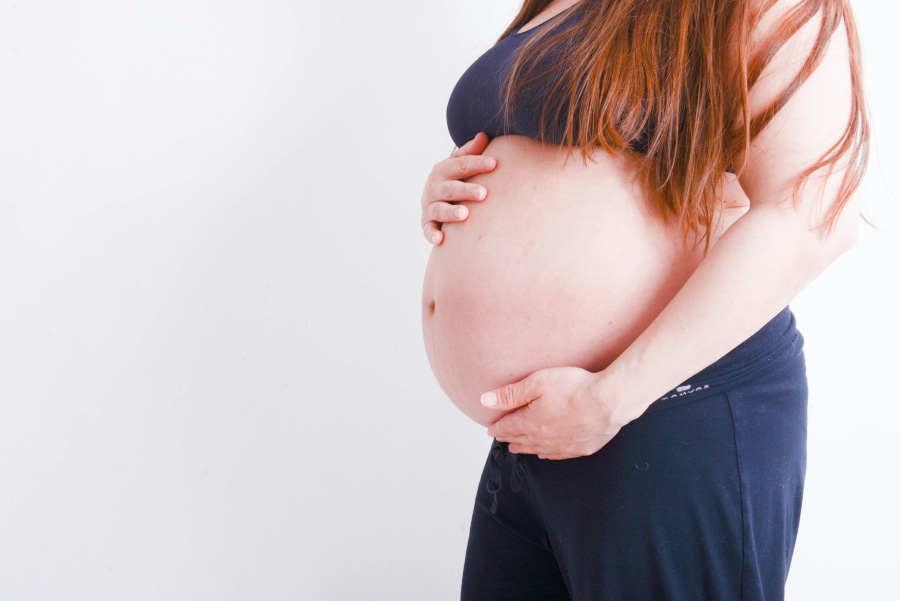 임신을 한 여성이 청색 바지와 브라를 입고 임신을 해서 배가 많이 불러 있는 것을 양쪽 손으로 감싸며 찍은 사진