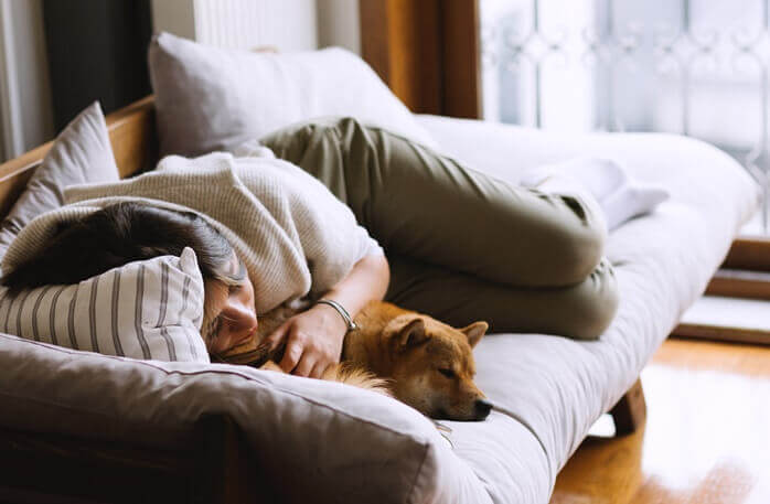 한 여자가 소파 위에서 강아지와 함께 자고 있는 모습