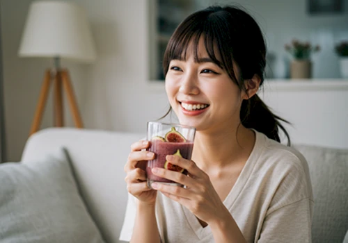 햇살 드는 거실에서 무화과 스무디를 마시며 활짝 웃는 한국인 여성. 건강하고 활기찬 생활 방식을 강조하는 모습입니다.