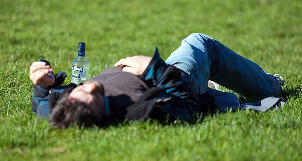 잔디 위에서 술병을 옆에 둔 채 누워있는 남자 사진