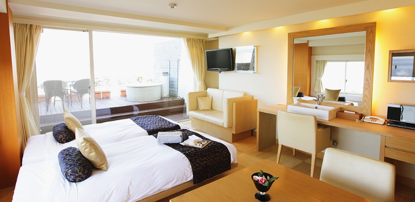 일본 호텔 내부 침대 2개와 테이블 소파 그리고 야외 테라스가 보인다