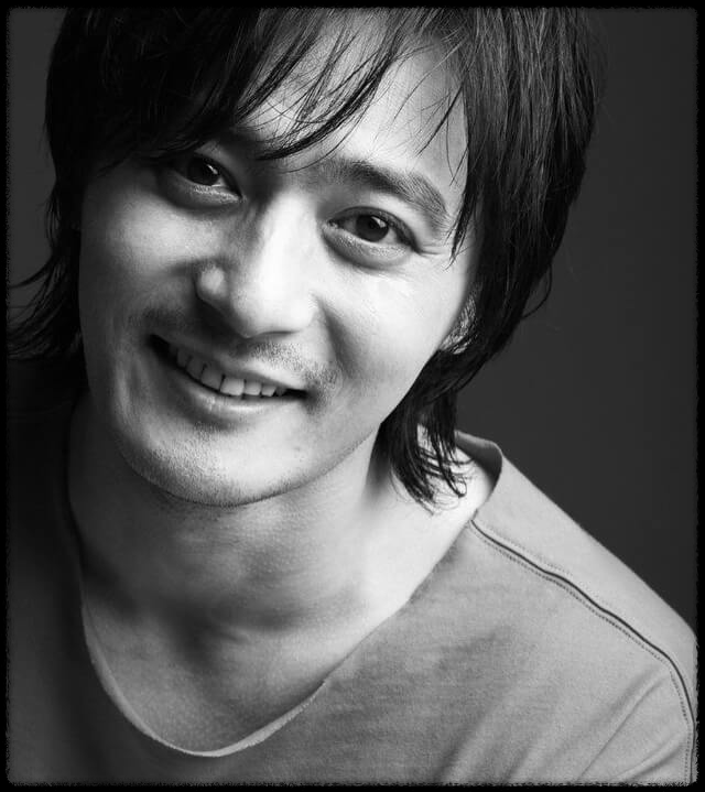 배우 장동건이 웃고 있는 모습. 흑백사진이다.