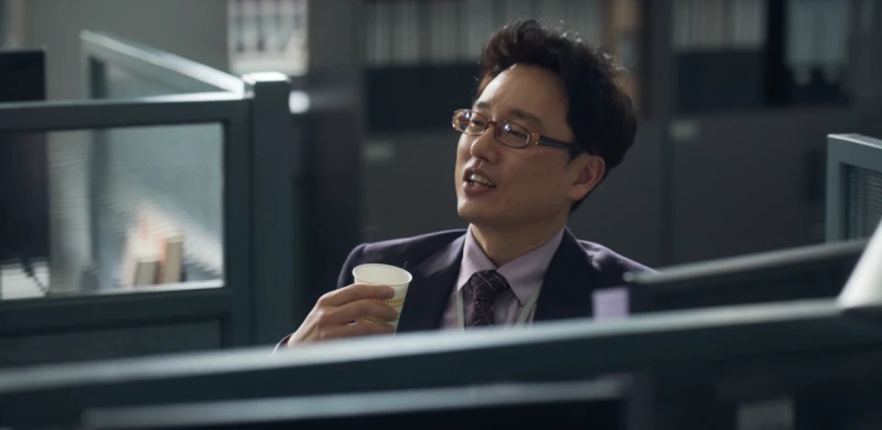사무실을 배경으로 책상에 앉아 한손에는 커피가 든 종이컵을 들고 있는 드라마 마스크걸의 차장 캐릭터