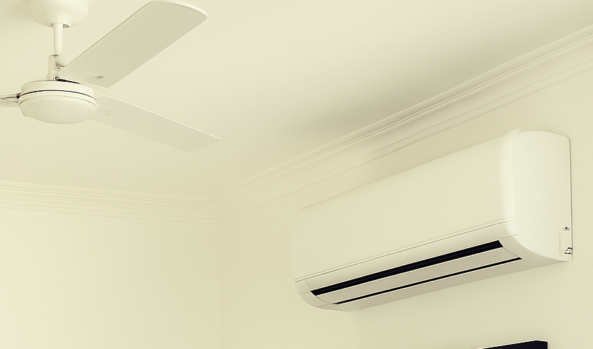 A photograph showcases a modern bedroom during daytime with a wall-mounted air conditioner above the bed, emphasizing a clean and well-ventilated indoor environment ideal for summer cooling.