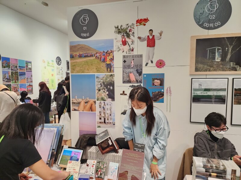 이와신 작가님 부스(1호) 빨간 한복 조끼와 흰 저고리&#44; 바지를 입은 모방 영감의 포스터가 벽에 붙어 있다.