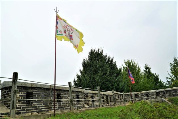 굽어진 성곽&#44; 왼쪽에 우뚝 솟은 노란 깃발&#44; 우측엔 붉은 깃발&#44; 흐린 하늘&#44;