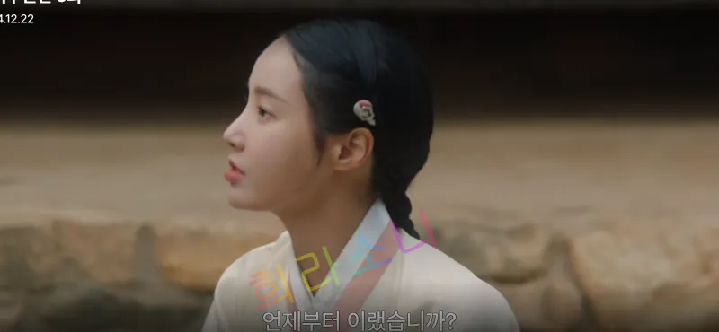 미령이 흰색 한복을 입고 정면이 아닌 측면을 바라보고 있다. 단정히 묶은 머리에는 작고 단아한 장식이 꽂혀 있다. 배경은 전통 한옥의 마당으로 보인다. 자막은 