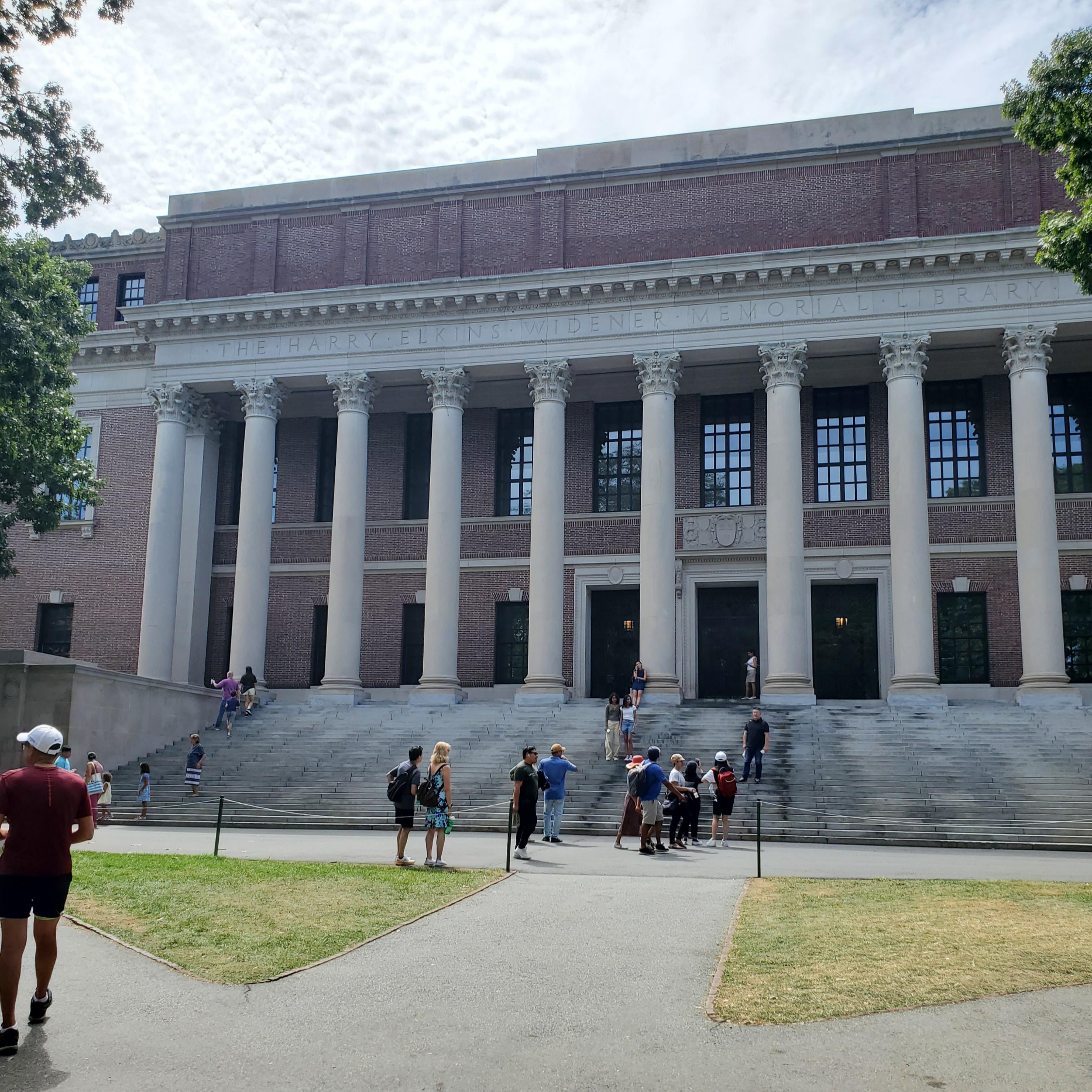 하버드 대학교 도서관 앞에서 찍은 사진. 자주색 벽돌 건물로 기둥들이 여러개 있고 앞에는 여러개의 계단이있습니다.