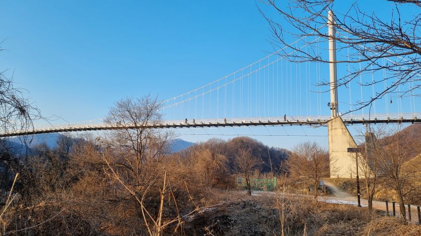 푸른 하늘에 가로 지른 출렁다리&#44; 사장교&#44; 삼각형 강선줄을 떠받치고 있는 가운데 주탑(철봉)&#44; 걸어가는 사람들&#44; 메뚜기만하게 보임&#44;