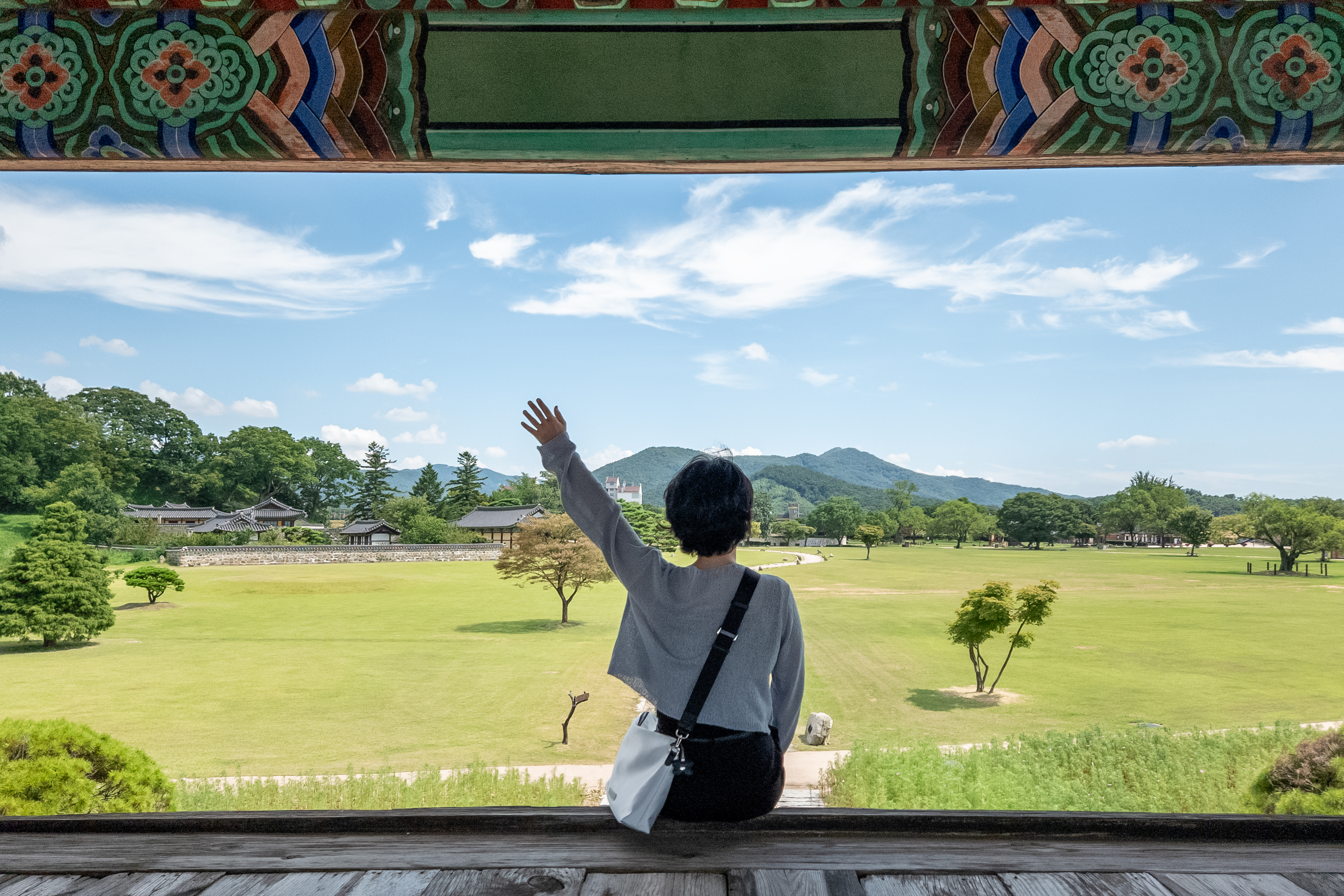 녹색 잔디밭을 바라보며 정자에 앉아 왼쪽 팔을 올린 사람