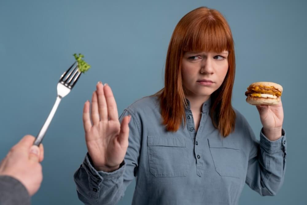 여자가 한손에 햄버거를 들고 채소를 거부하는 모습