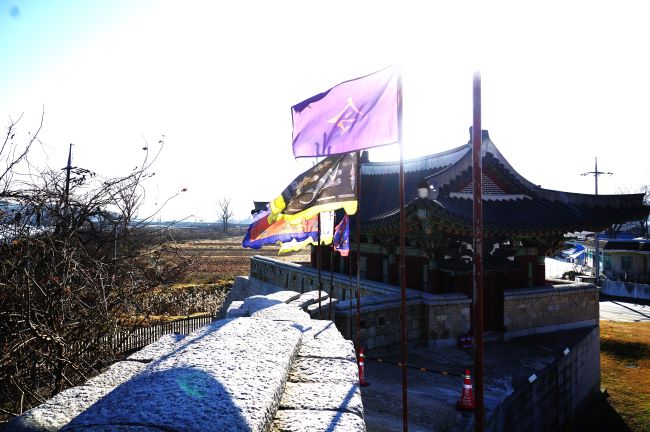 조해루의 역광 사진, 펄럭이는 깃발에 강렬하게 비치는 햇빛, 성곽 돌담에 드리운 선명한 그림자,