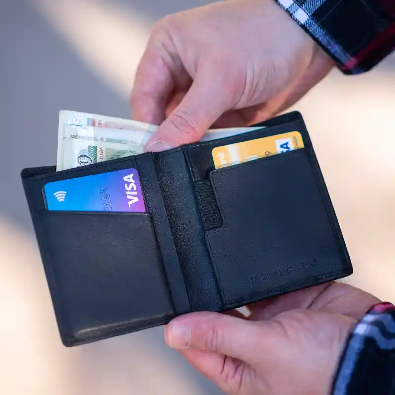 한 남성이 검정색 반지갑에서 현금을 꺼내고 있는데&#44; 지갑 앞 포켓에는 신용카드가 두 장 들어 있다.