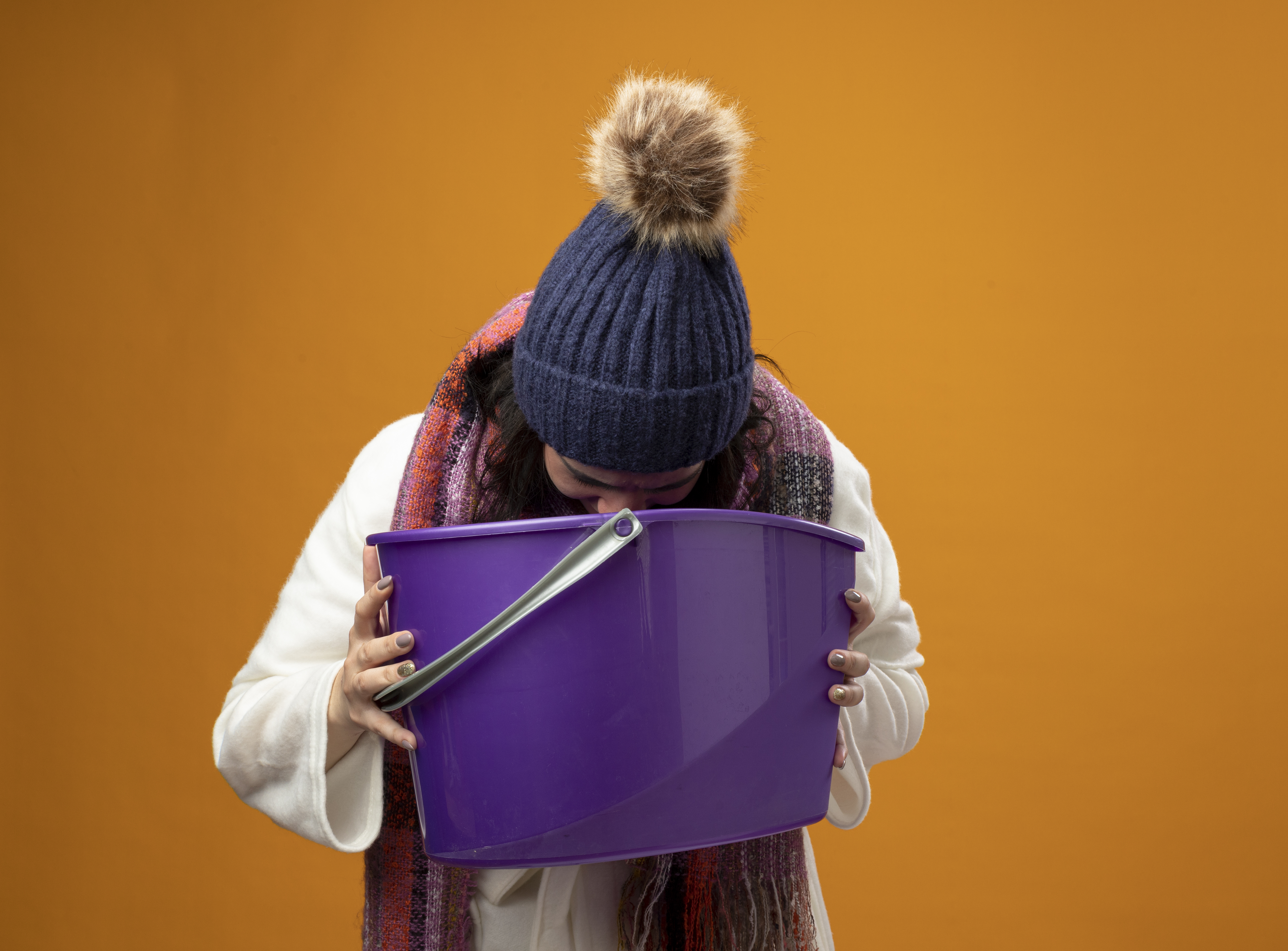 young-ill-woman-wearing-robe-winter-hat-scarf-having-nausea-holding-plastic-bucket-vomiting-into-it-isolated-orange-wall