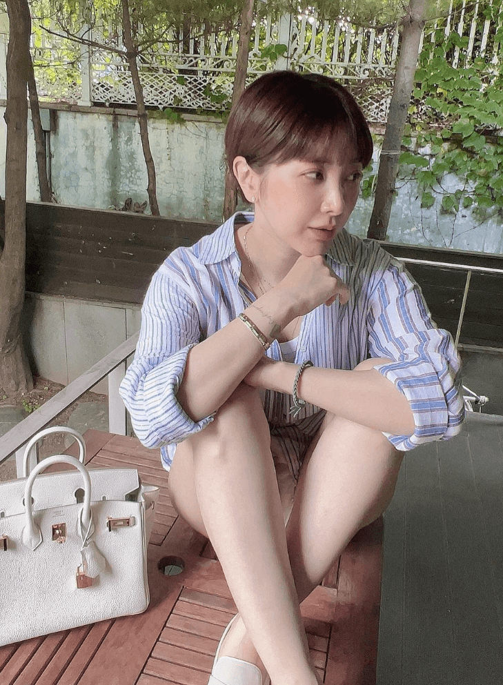 서인영이 야외 반바지와 하얀색 와이셔츠를 입고 야외 벤치에 쪼그려 앉아있다.