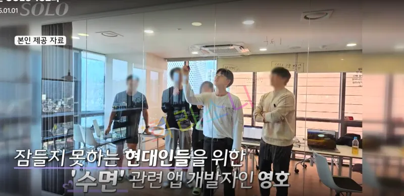 실내 회의실에서 여러 명의 사람들이 회의를 진행하고 있다. 24기 영호가 유리 칠판에 무언가를 작성하고 있으며&amp;#44; 나머지 사람들은 서 있거나 대화를 나누고 있다. 화면 하단에는 
