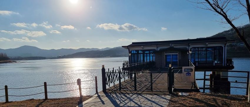단층 수상 건물, 잠겨 있는 출입구, 뒤로 드넓은 호수, 둘러쳐진 야산, 푸른 하늘, 흰구름, 역광,