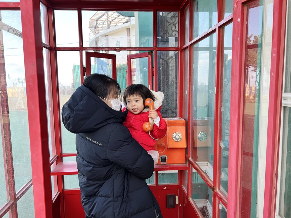 입구 앞에 있는 빨간 공중전화 부스에서 전화받는 척 하는 아기