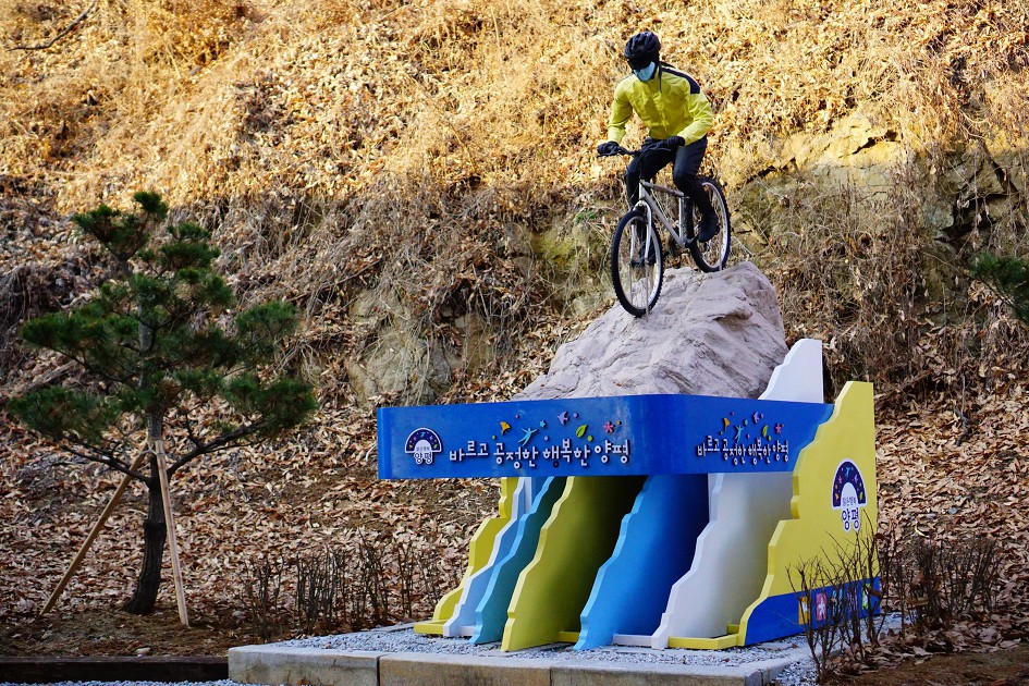 바위 위에 만들어 놓은 자전거 타는 남자 조형물&#44; 노란 자켓&#44;