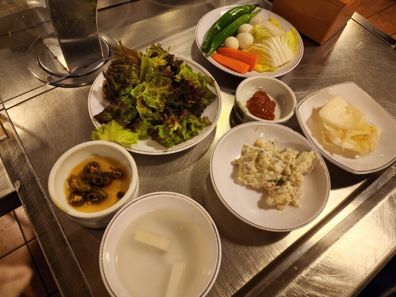 기본 세팅되는 밑반찬. 백김치&#44;고추장아찌&#44; 상추 겉절이&#44; 감자샐러드&#44; 메추리알과 당근 등의 야채가 서빙된다.