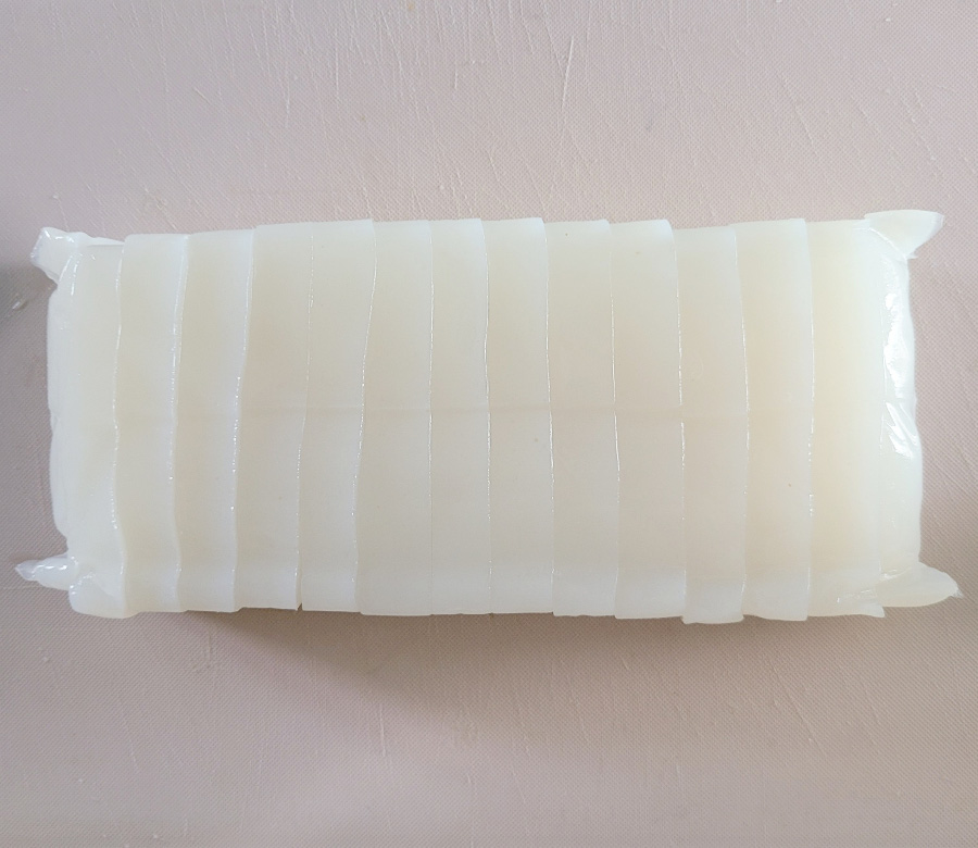흰색의 곤약을 하얀 바닥 위에 한 덩어리 놓아두고 먹기 좋게 칼로 썰어놓은 것을 위에서 찍은 사진