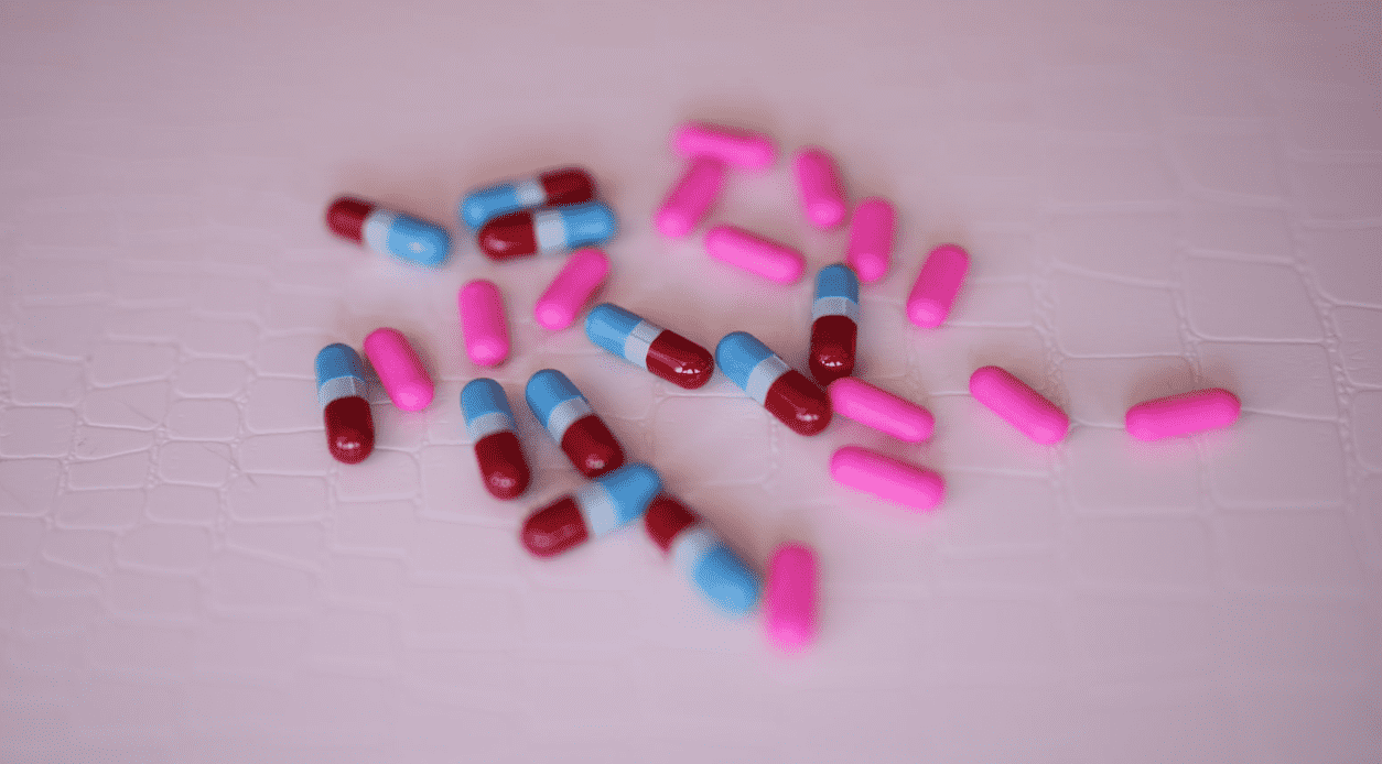 Pills made for something are placed on a nice purple table. Pills are blue white red and pink capsules.