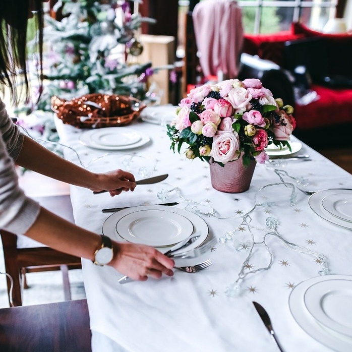 예쁜 꽃이 있는 식탁에 빈 접시와 포크, 나이프를 놓으며 식사 준비하고 있는 여자