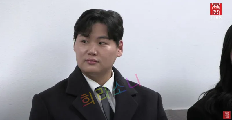 검은색 코트를 입은 23기 영호가 흰 벽 앞에서 고개를 살짝 돌리고 있는 모습이다. 뒤에는 긴 머리를 풀어내린 여성이 보인다. 화면 오른쪽 상단에는 '촌장 LIVE' 로고가 보인다. 자막은 '희라소니'라고 적혀 있다.