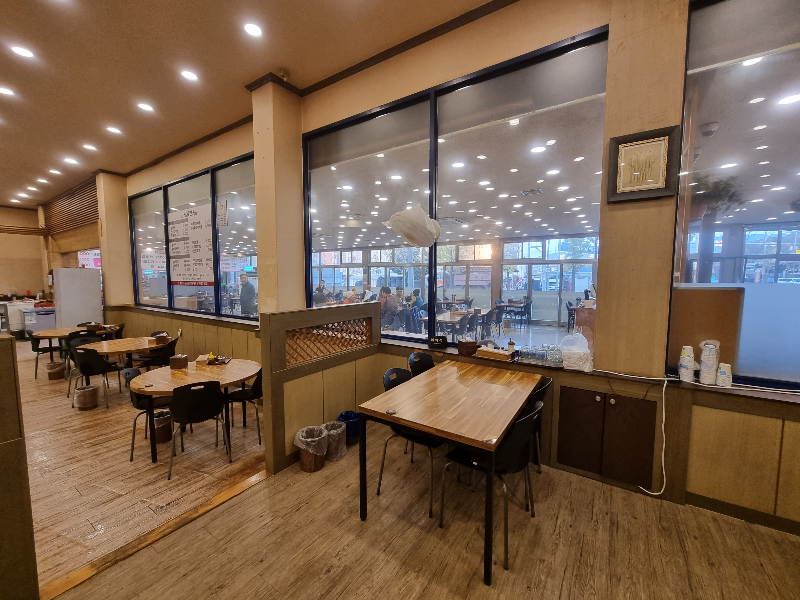 또다른 식당내부 모습으로 가운데 유리로 된 벽이 쳐져있어 공간이 분리되고 원형 테이블과 3개&#44; 사각테이블 1개와 검은색 의자들이 있는 모습