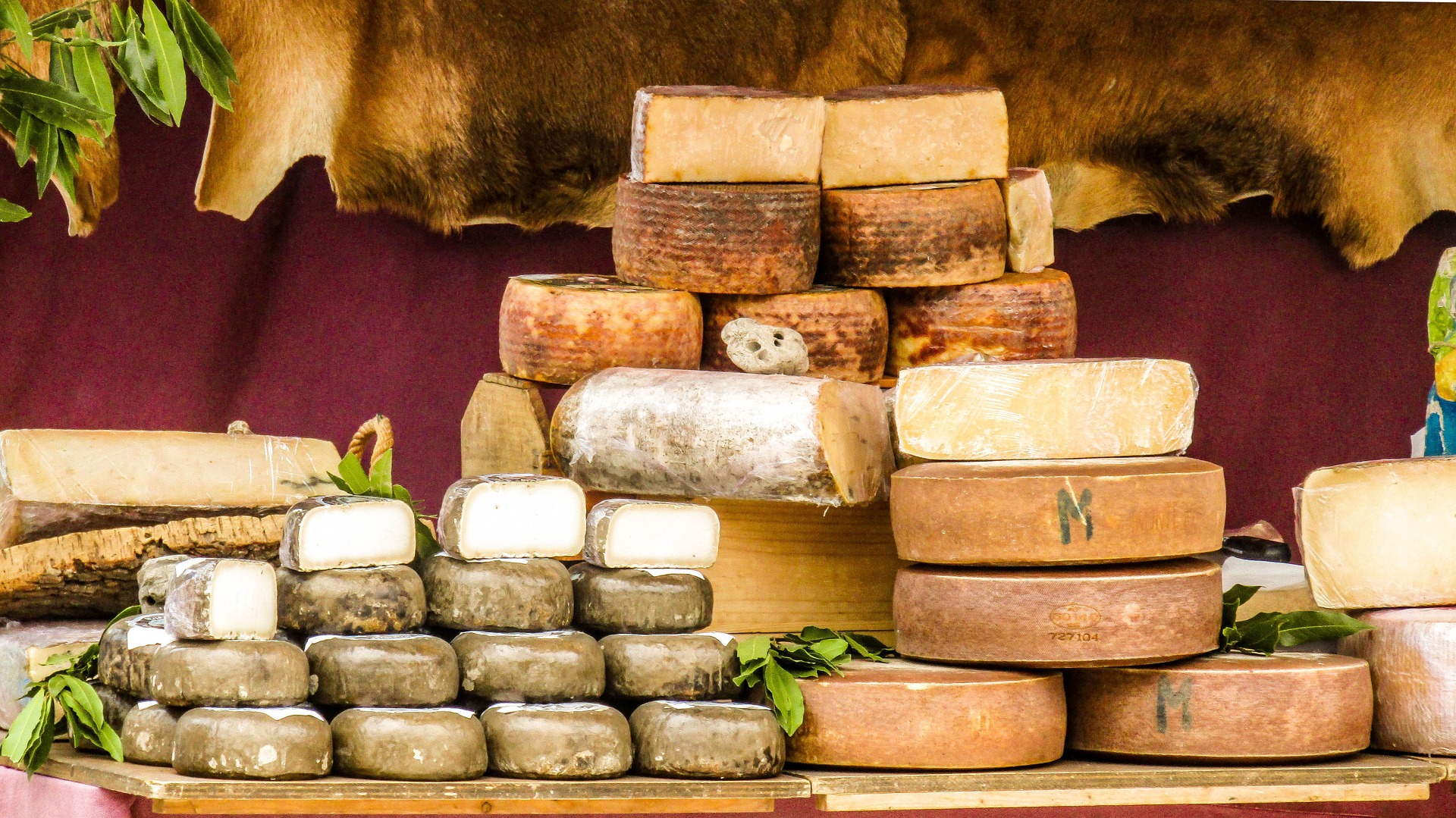 나무로 된 테이블 위에 여러 가지 동그란 치즈를 종류별로 수북하게 쌓아 놓고 찍은 사진