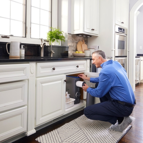 A person demonstrating the DIY process of changing a reverse osmosis filter in a kitchen, showcasing tools and a new filter.