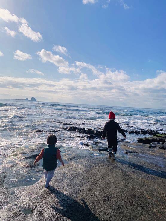 사계해변의 화산석 위에 아이 2명이 걷고 있는 사진이다.
화산석 위로 바다가 치고 하늘은 약간의 구름만 있고 매우 화창하다.