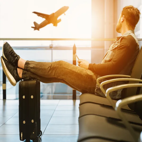 공항 내부에서 창밖에 날아가는 비행기를 보고 있는 남성