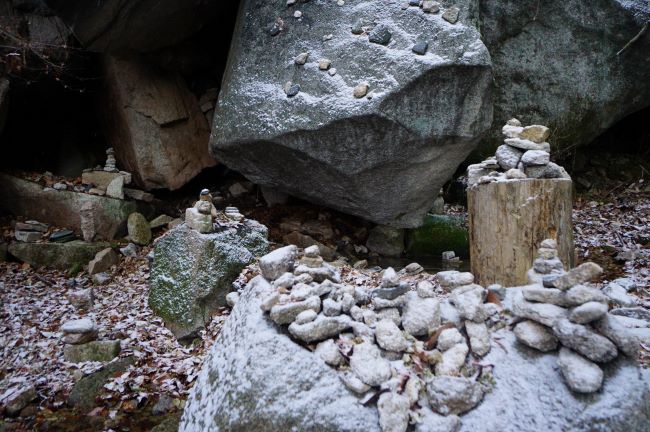 큰바위 위에 돌 몇 개씩 쌓아 놓아 만든 돌탑 여러개에 하얀 눈이 쌓여 있음&#44;