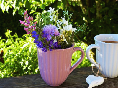 보라색&#44; 흰색&#44; 분홍색 들꽃이 꽂혀 있는 컵 옆에 커피가 담겨 있는 흰색 컵