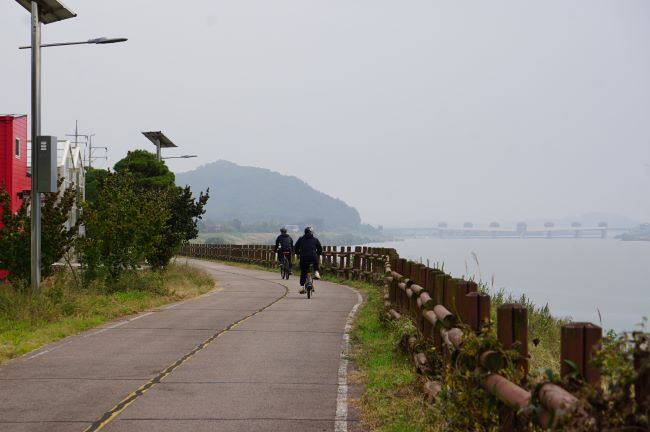 자전거 타고 지나가는 남자 2&#44; 검은 옷&#44; 우측에 희미한 남한강&#44; 흐린 하늘&#44;